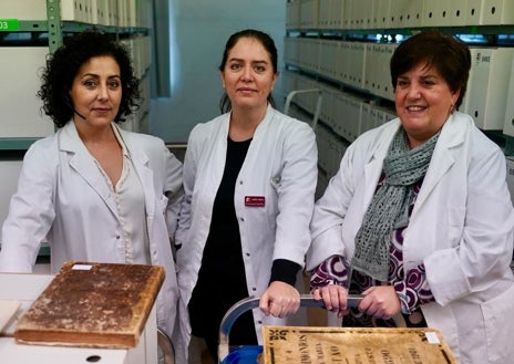 Imagen secundaria 1 - Un momento del proceso de transcripción digital de la partida de nacimiento contenida en uno de los libros en el archivo de la Iglesia en Vizcaya, en la foto superior. Debajo, las tres archiveras encargadas de esta institución, una de las pocas que tiene indexados los archivos hasta 1900. En el detalle, varios libros y junto a las partidas que han sido transcritas. 