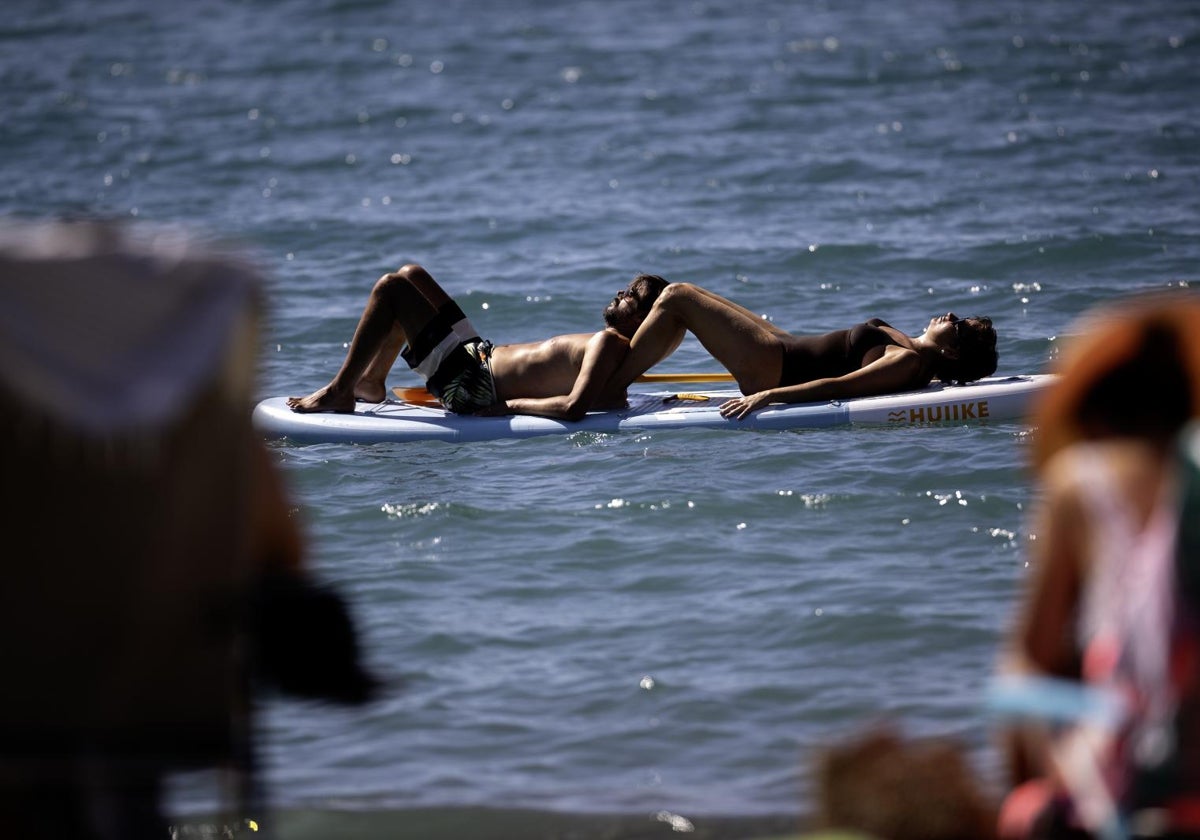 Varias personas toman el sol en una tabla de surf en la playa de la Malagueta en Málaga