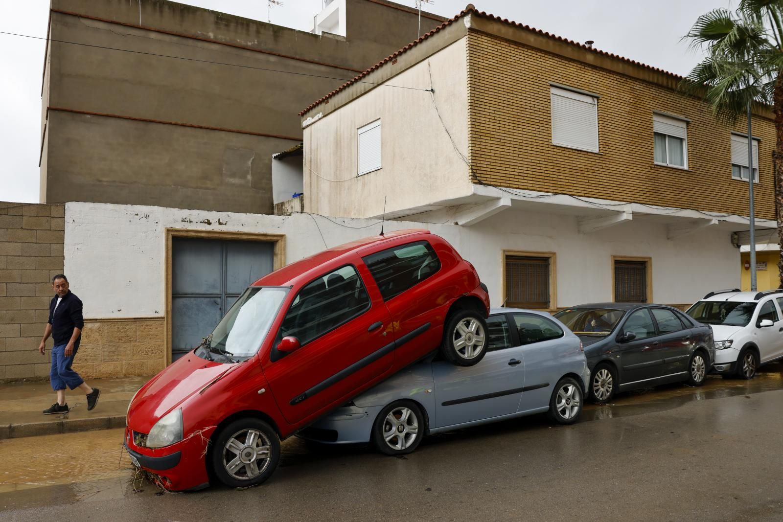 Una persona pasa junto a unos coches amontonados debido a las lluvias torrenciales que afectan a la Comunitad Valenciana