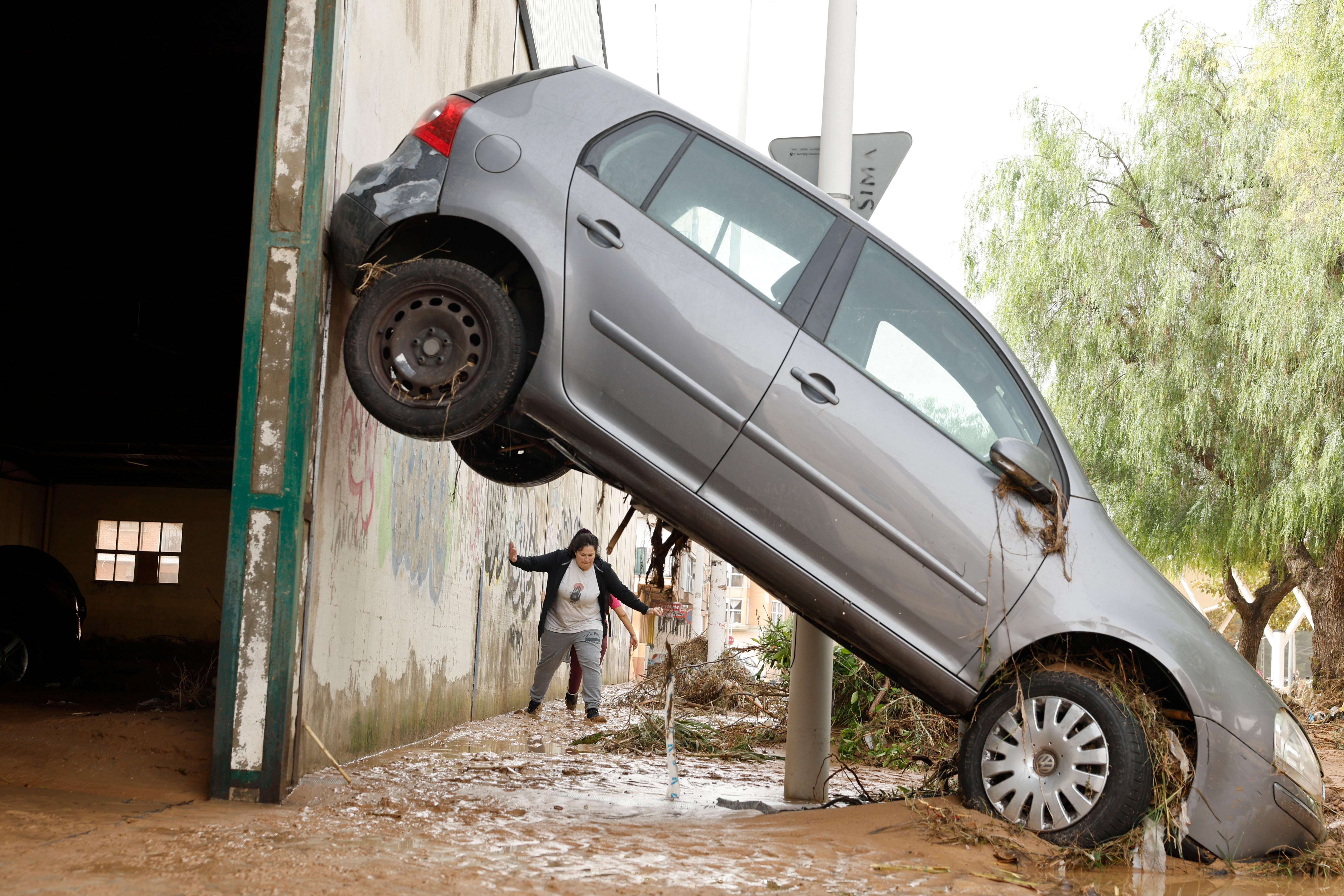 Una persona entre el barro mira como un coche se ha quedado encajado contra una pared