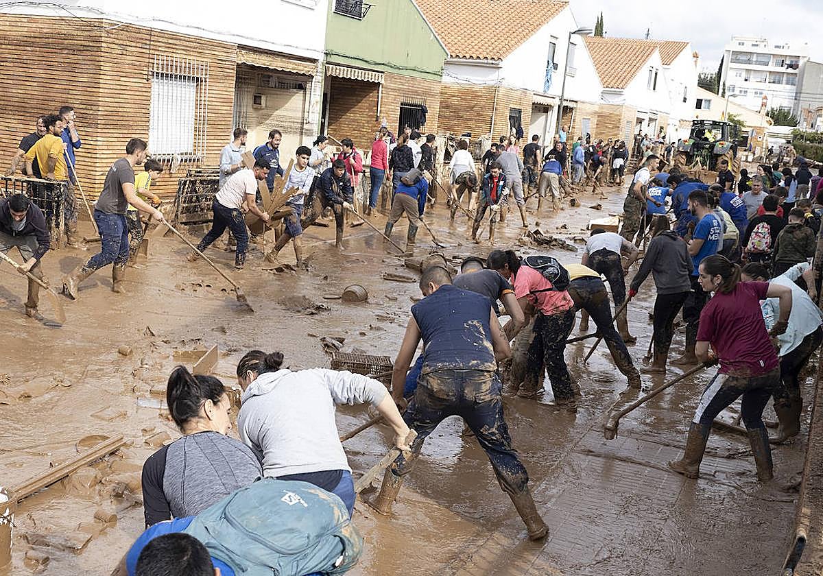 Varias personas colaboran en la limpeza de una calle afectada en la localidad de Utiel