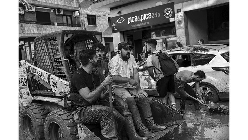 Un grupo de voluntarios sobre la pala de un tractor en la calles de Paiporta