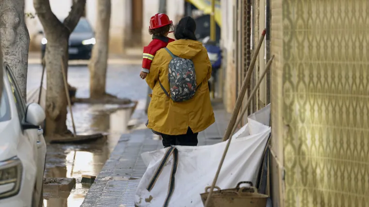 Una mujer lleva en brazos a un niño disfrazado de bombero por una calle en la localidad valenciana de Masanasa