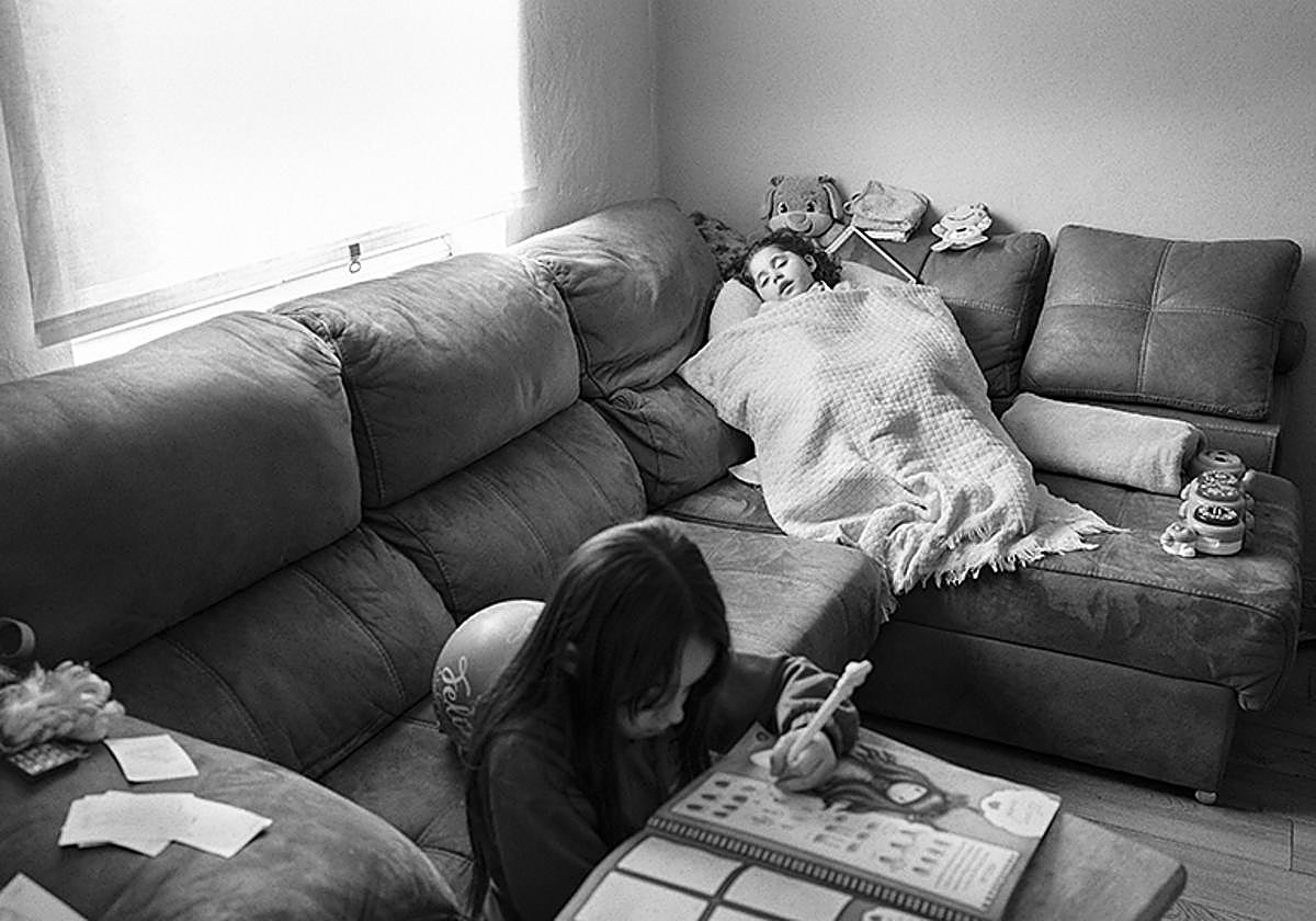 Avilés, Asturias - 15 Enero 2025: Kaila (al fondo de la imagen), enferma de leucodistrofia, reposa en el sofá de su casa mientras su hermana Xenia le hace compañía y dibuja en uno de sus cuadernos