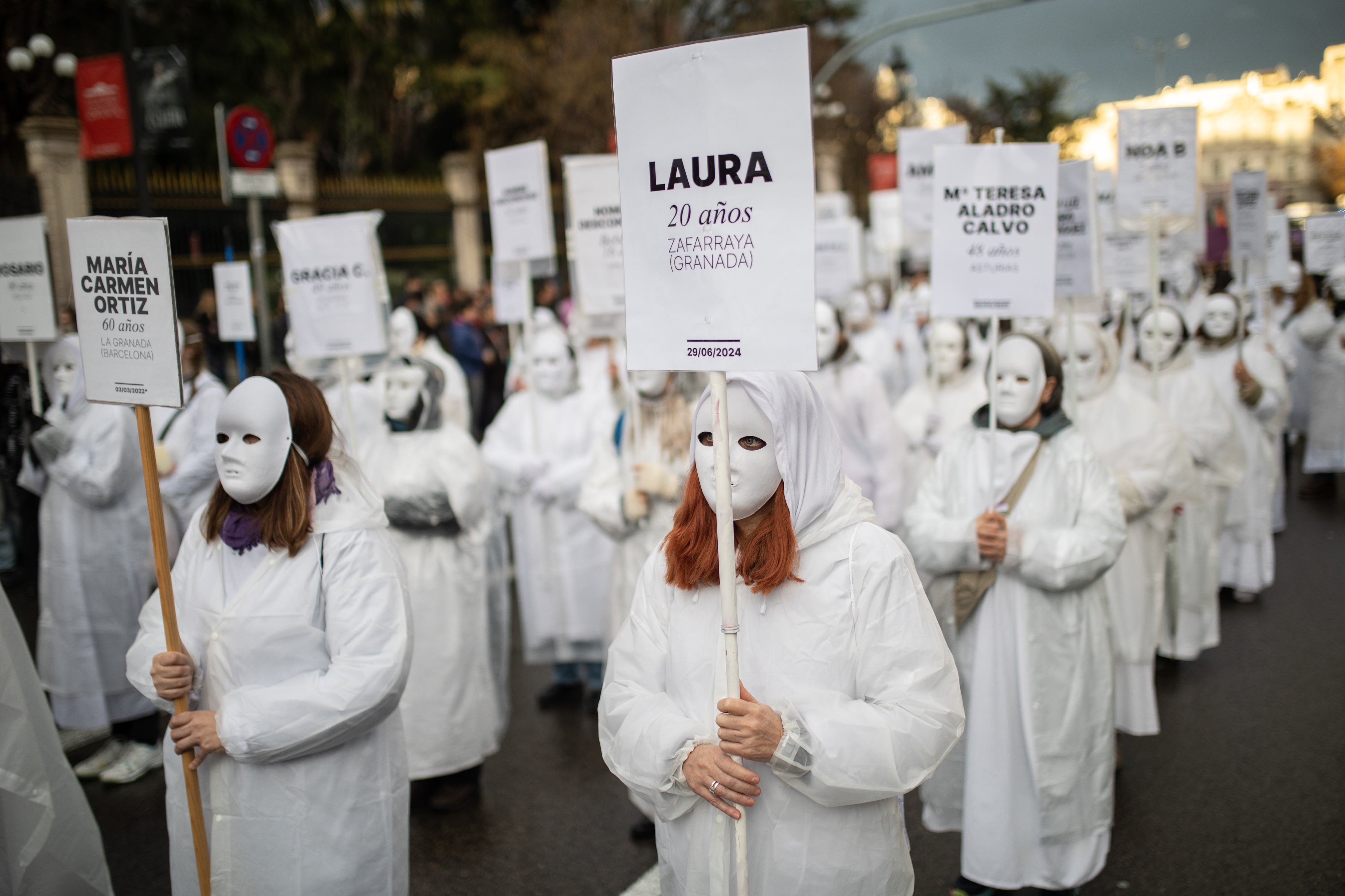 Manifestantes sin rostro, con carteles con los nombres y edades de las mujeres asesinadas en la manifestación convocada por el Movimiento Feminista de Madrid por el 8M