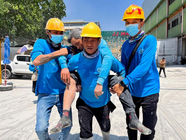 Varios trabajadores transportan a una persona herida cerca del lugar donde se derrumbó un edificio en Myanmar