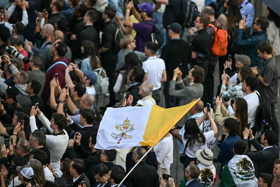 Grupos de personas con la bandera del Vaticano en la Plaza de San Pedro esperando a la segunda fumata, la primera de la mañana de este jueves.