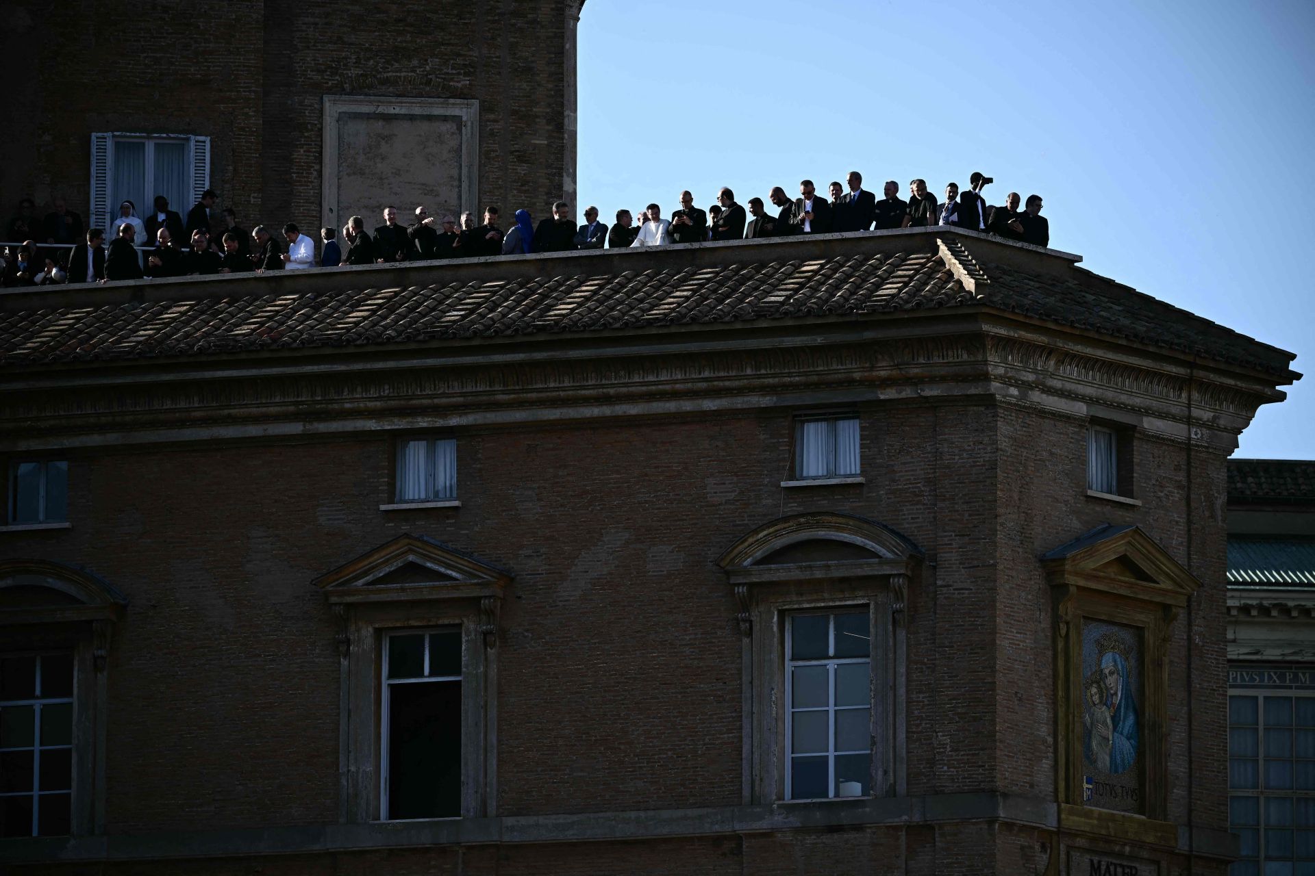Grupos de personas esperan en una azotea a la primera aparición del Papa.