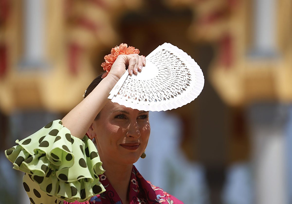 Una mujer vestida de flamenca se cubre los ojos con un abanico ante el calor que golpea en España