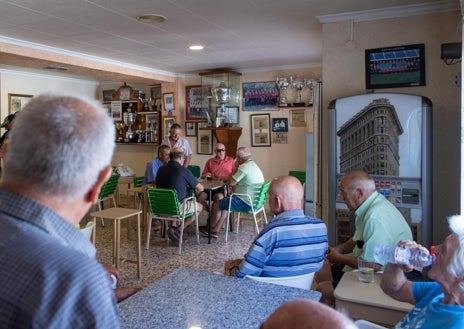 Imagen secundaria 1 - En la foto superior está jugando una partida de dominó. En la imagen central, conversa con los vecinos del pueblo en el bar. En la tercera, pide su cortado en la barra.