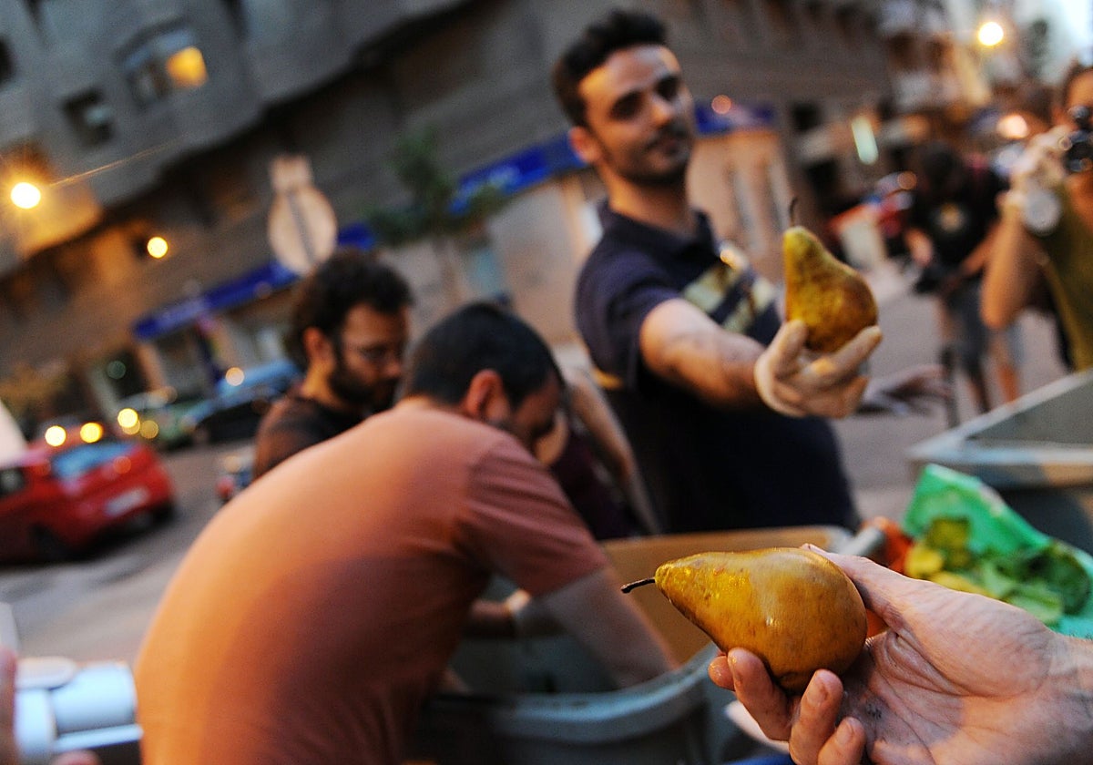Miembros del grupo activista «Comida Basura», que busca concienciar sobre el desperdicio de alimentos, muestran peras sacadas de los cubos de basura fuera de una tienda, en Madrid