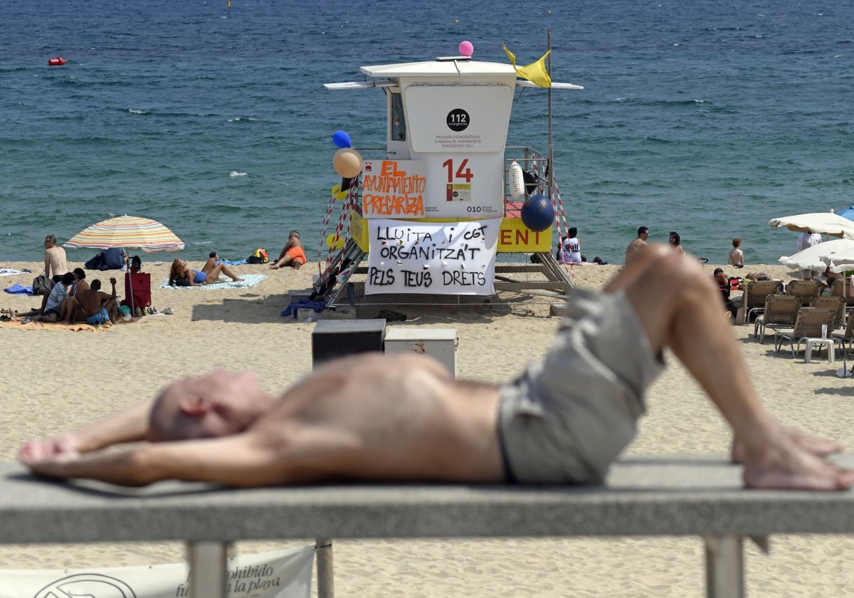 Un hombre toma el sol frente al puesto de socorrismo de una playa de Barcelona, cerrado por huelga