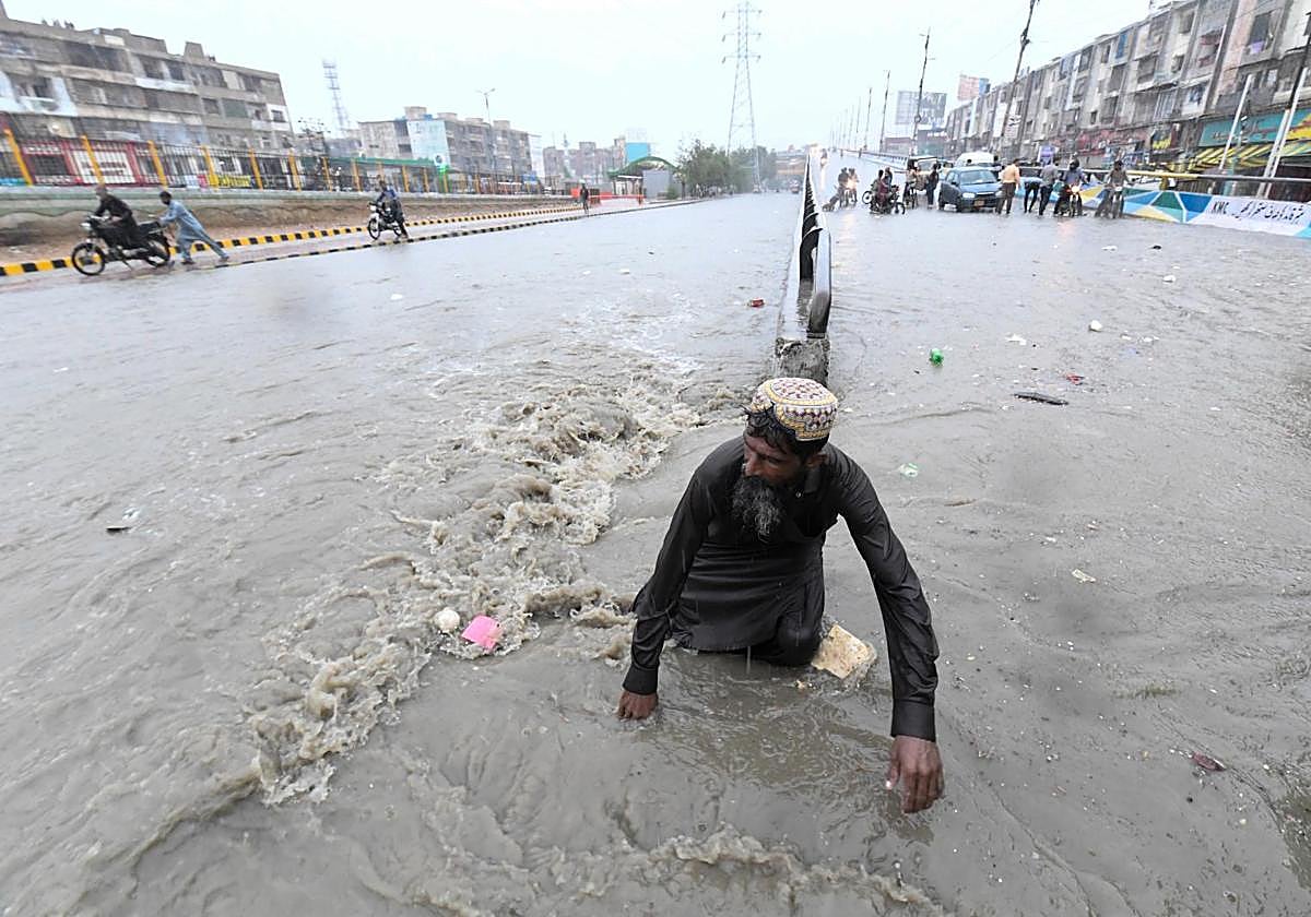 Un hombre transita una calle inundada por fuertes lluvias monzónicas en Karachi