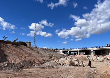 Imagen secundaria 1 - En la imagen superior, la zona de la valla de protección del caudalímetro que no fue derribada por la riada todavía tiene cañas y matorrales acumulados, el resto está en el suelo, semienterrada. En la segunda imagen se puede observar la caseta del caudalímetro, a la izquierda, y el puente de la A3 que pasa por encima del barranco del Poyo. Un cable une el poste de la instalación con el sensor láser  instalado en el puente. En la tercera imagen, un primer plano de la caseta y las placas solares que la alimentan,