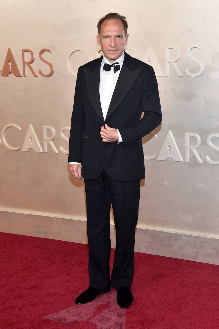 Ralph Fiennes con esmoquin, con camisa blanca y una original pajarita negra y ribeteada en blanco. 