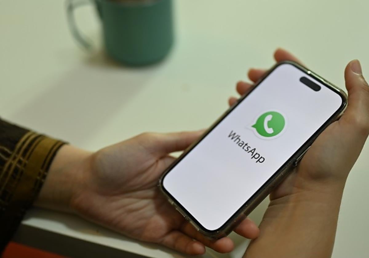 Mujer sujetando un smartphone en cuya pantalla aparece el logo de WhatsApp