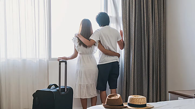 Una pareja de viajeros asomada a la ventana de la habituación de un hotel