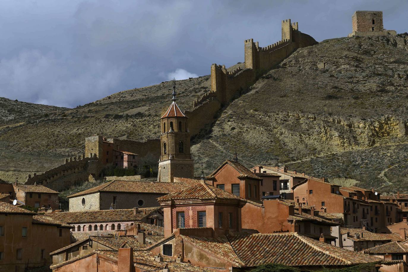 Albarracín, Teruel. Mientras que la primera planta de las casas es de mampostería (algunas con esquinas de piedra), los pisos altos muestran entramado de yeso y madera, y las calles conservan el empedrado antiguo. A un guerrero moro, Ben Razin, debe su nombre. Pero ya antes, este refugio natural había sido utilizado por el hombre prehistórico, que dejó pinturas rupestres en algunas cuevas próximas. También sirvió de escondite a pastores huidos de los romanos. Los visigodos la llamaron Santa María del Levante y los árabes la hicieron capital de un reino, y levantaron castillo y murallas. Muchas de las torres pertenecen a aquella época (siglo X). Escenario de numerosas luchas entre moros y cristianos, está rodeada de murallas que protegen su parte antigua. La catedral alberga retablos del siglo XVI, y el museo colección de tapices. No hay que irse sin fotografiar la inclinada casa de Julianeta, la imagen más difundida de la villa.