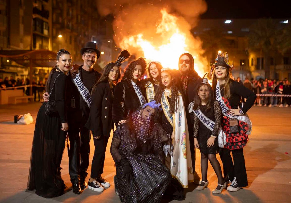 La corte carnavalera posa junto a la pira donde se consume el choco