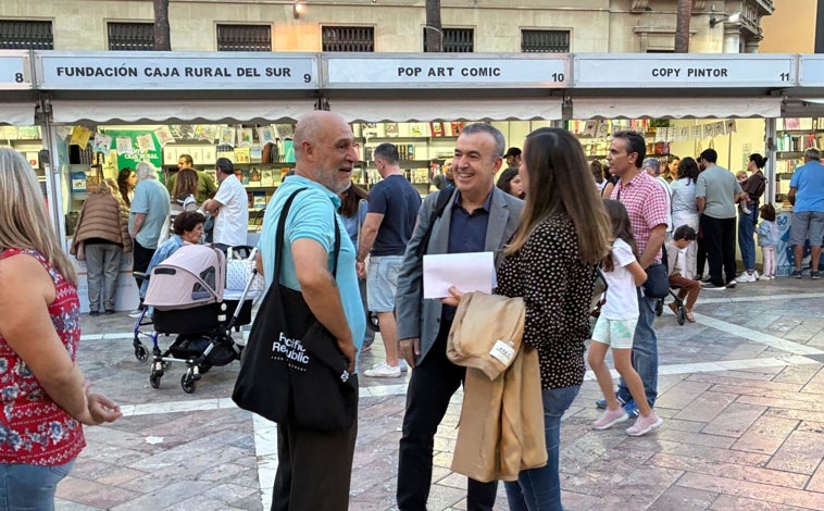 Imagen principal - Lorenzo Silva, en la plaza conversando con el autor onubense Mario Marín y en su encuentro con los lectores. / Luis Alfonso Morales firmando su primera obra, 'Huelvalogía'
