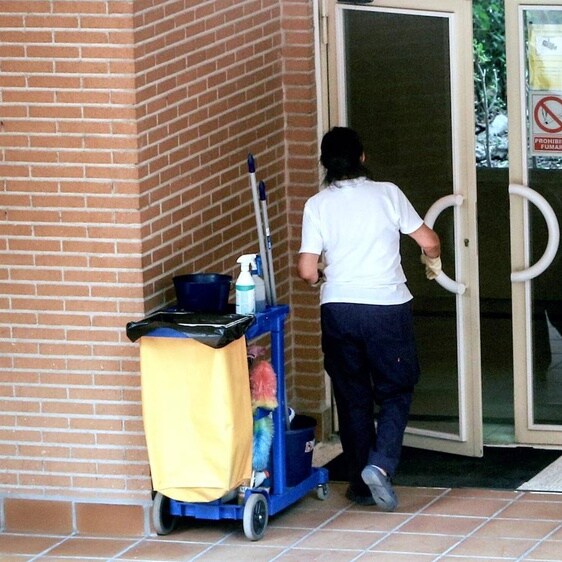 Una trabajadora de la limpieza entra en un edificio con el carrito de la limpieza