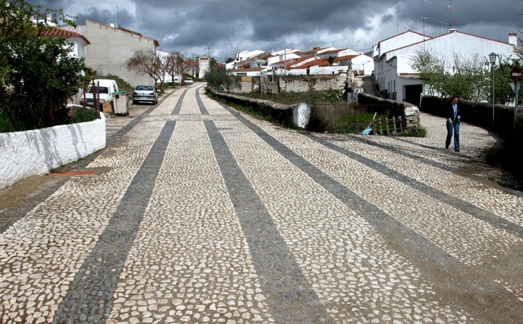 Imagen principal - En la imagen superior, una calle de Arroyomolinos; abajo y a la izquierda, un sendero coloreado con los tonos de otoño y a la derecha el hito que define el punto más alto de la provincia de Huelva