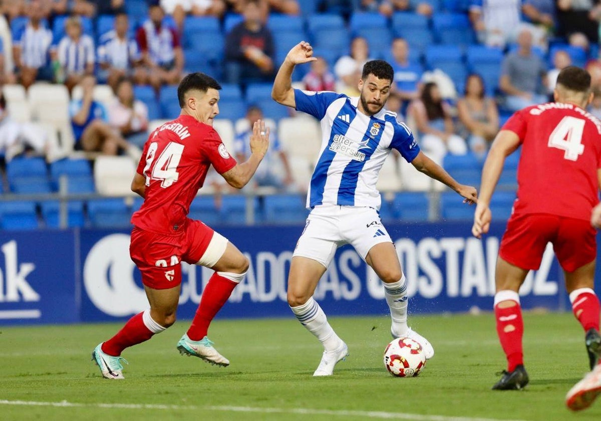 Luis Alcalde conduce el balón ante dos rivales del Sevilla Atlético