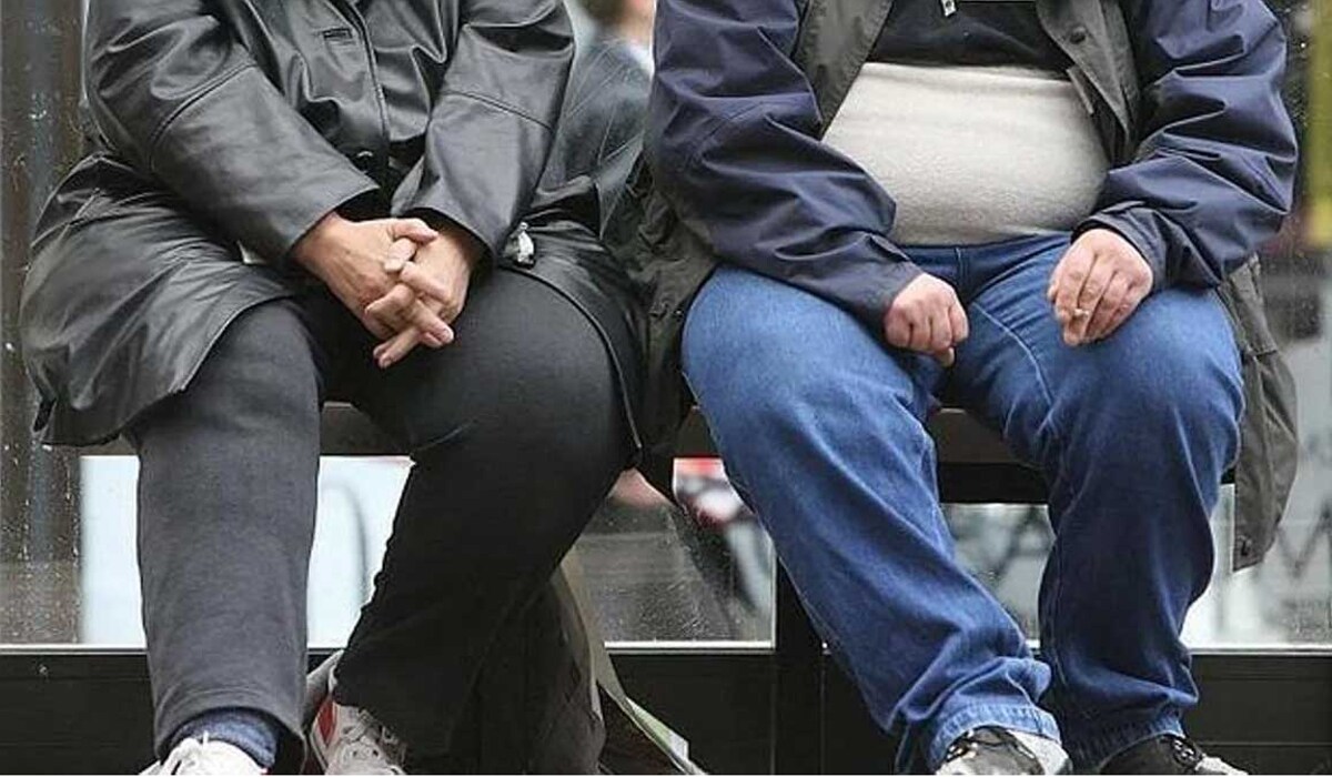Dos personas con exceso de peso en una parada de autobús