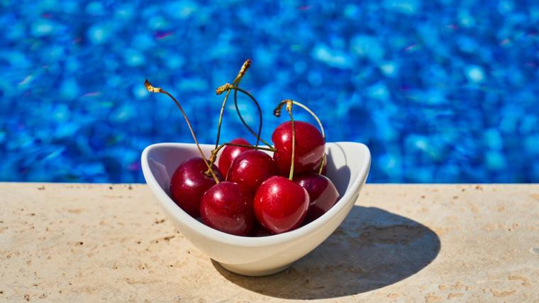 Imagen de un cuenco de cerezas junto a una piscina