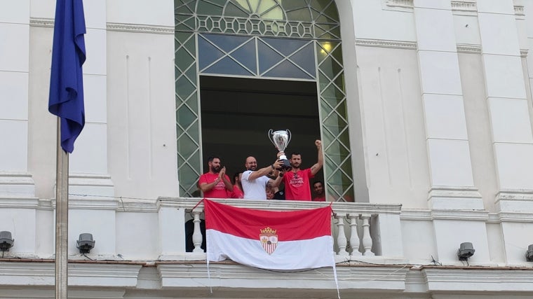 El alcalde Germán Beardo y el capitán Álex Colorado levantan la copa de campeón de Primera Andaluza en presencia del entrenador racinguista Juanjo Durán.