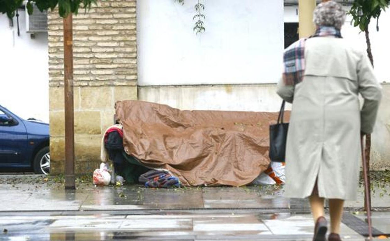 Una persona sin hogar se cubre de la lluvia en plena calle.