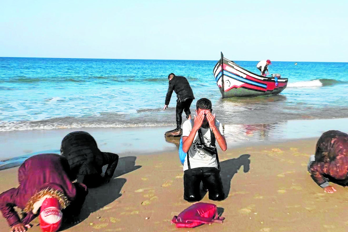 Unos migrantes rezan y dan gracias besando el suelo de la playa Victoria de Cádiz.