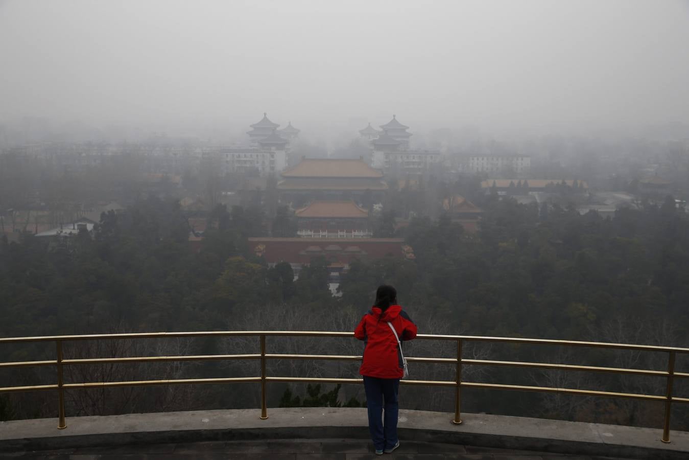 Una mujer observa el paisaje envuelto por una espesa niebla gris desde un mirador del parque Jingshan de Pekín (China)