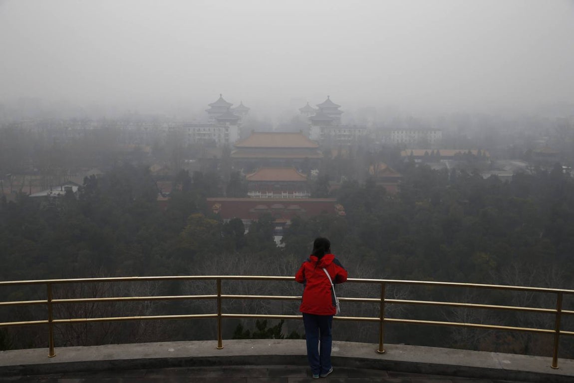 Una mujer observa el paisaje envuelto por una espesa niebla gris desde un mirador del parque Jingshan de Pekín (China)