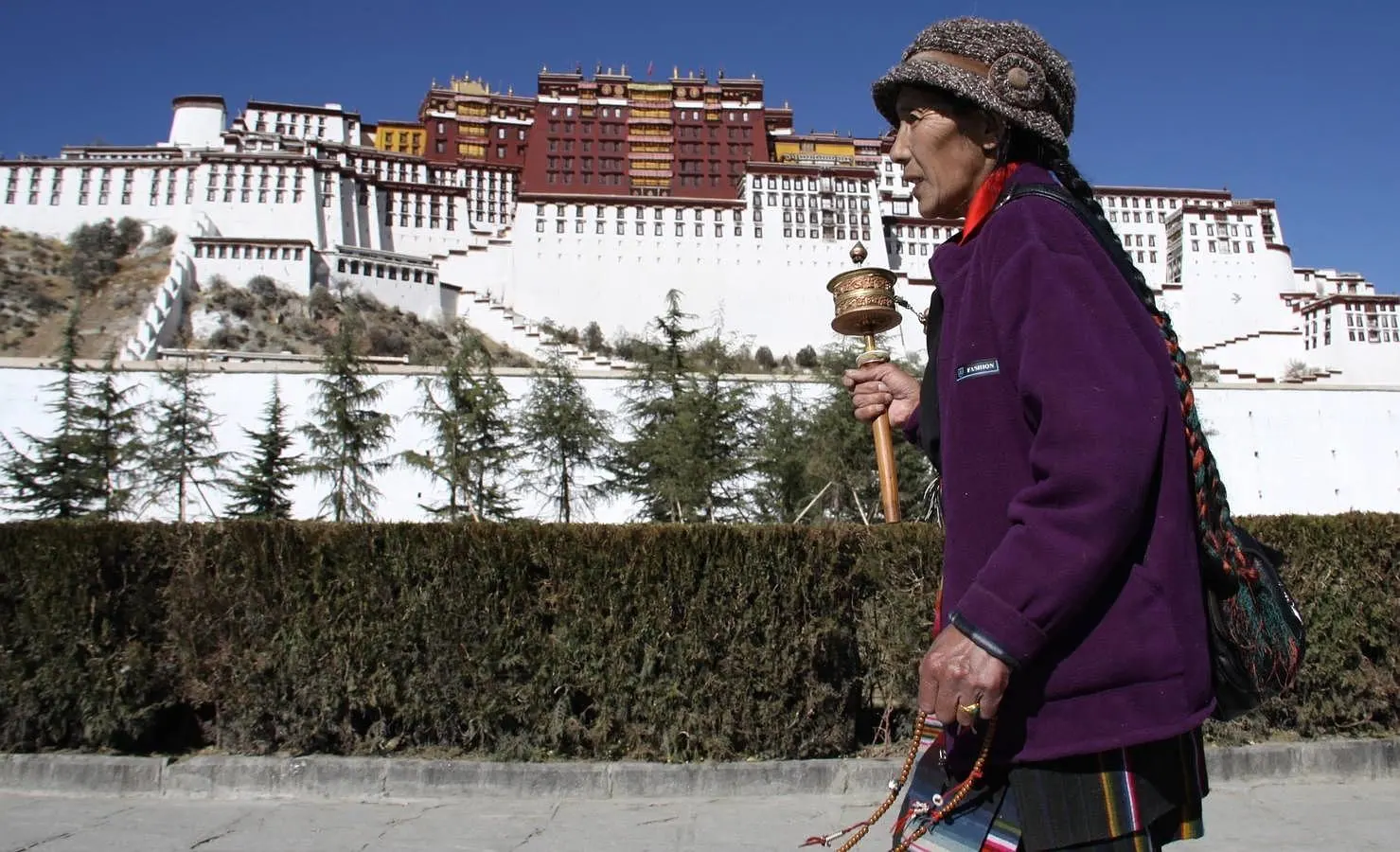 Dándole vueltas al molinillo de oraciones, una peregrina tibetana reza alrededor del Palacio de Potala, en Lhasa