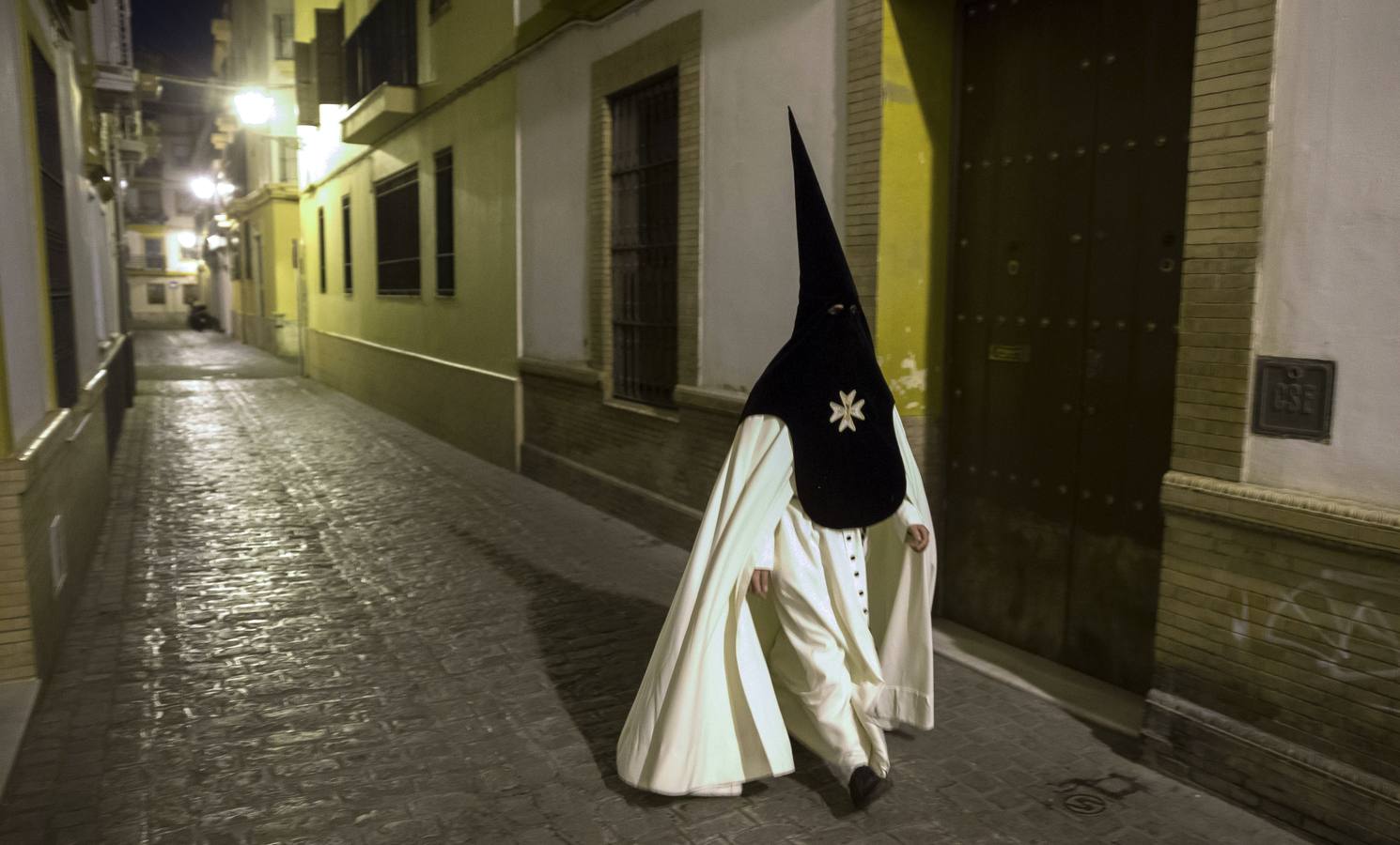 04. Un nazareno de la Hermandad de la Macarena camina por una calle solitaria camino del templo para el recorrido procesional por la calles de Sevilla en la tradicional "Madrugá".