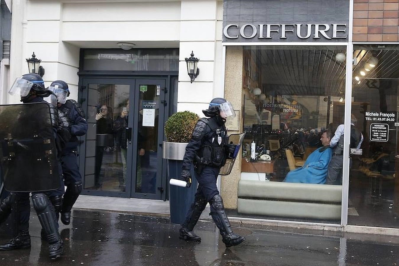 Clientes de una peluquería toma fotos a primera hora de la mañana mientras la policía toma posición ante las primeras marchas de protesta en París. 