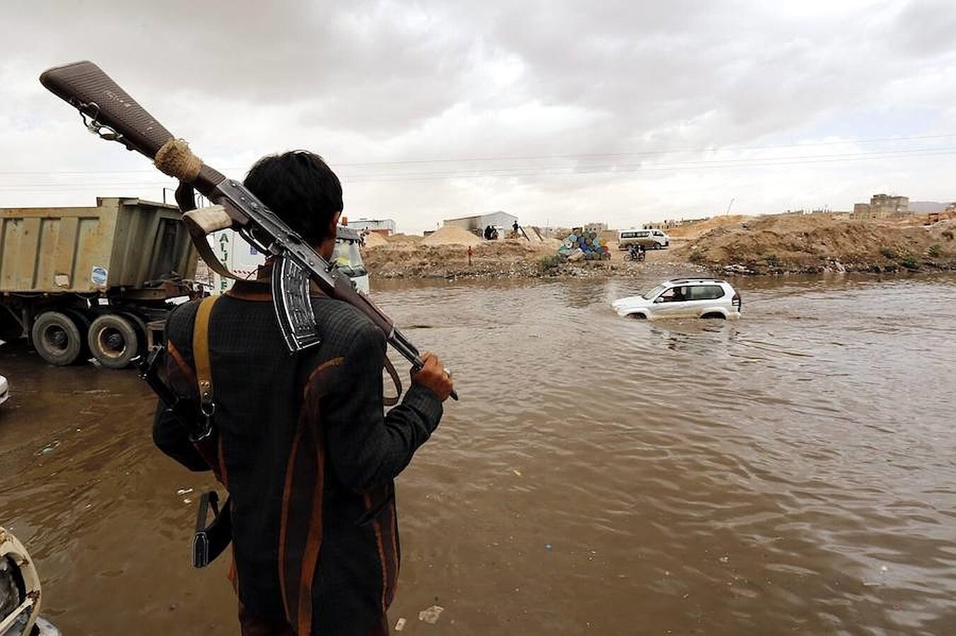 Un miliciano hutí observa un coche sumergido en una carretera inundada de Saná