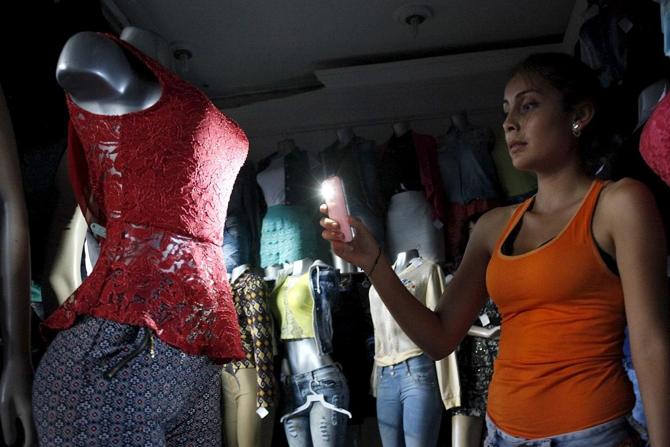 Una mujer utiliza su teléfono móvil para iluminar ropa en una tienda durante el apagón de luz en San Cristóbal, Venezuela