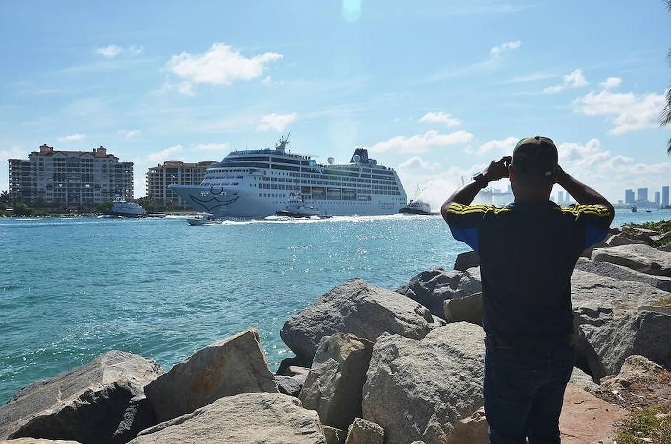 Un hombre toma desde tierra una fotografía a la embarcación de la compañía Fathom, filial de Carnival, el Adonia