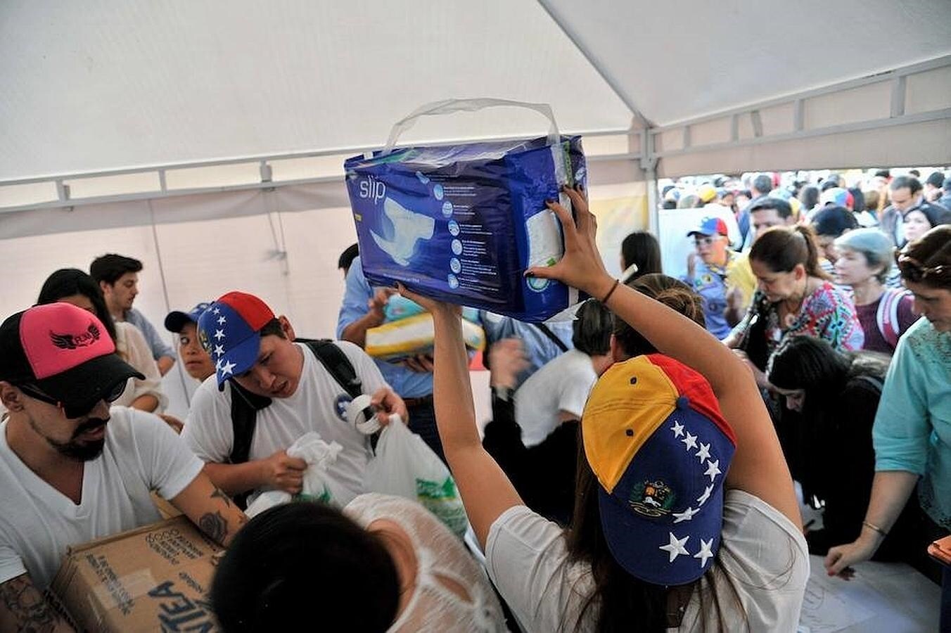 Una mujer sostiene una bolsa de pañales, mientras otros ciudadanos hacen cola para entregar sus donativos para el pueblo venezolano en una colecta liderada por Lilian Tintori en Bogotá