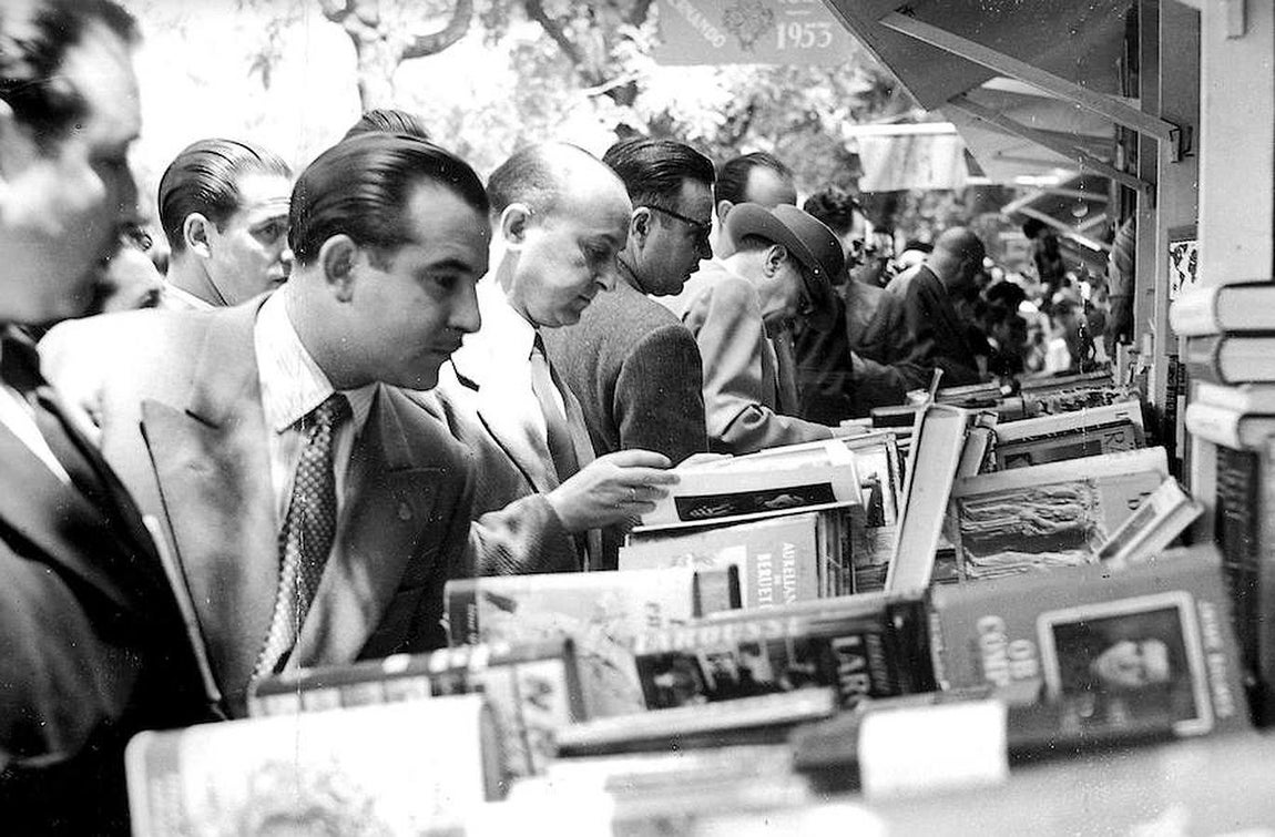 Asistentes a la feria en 1953, entonces en Recoletos, miran los libros expuestos. 