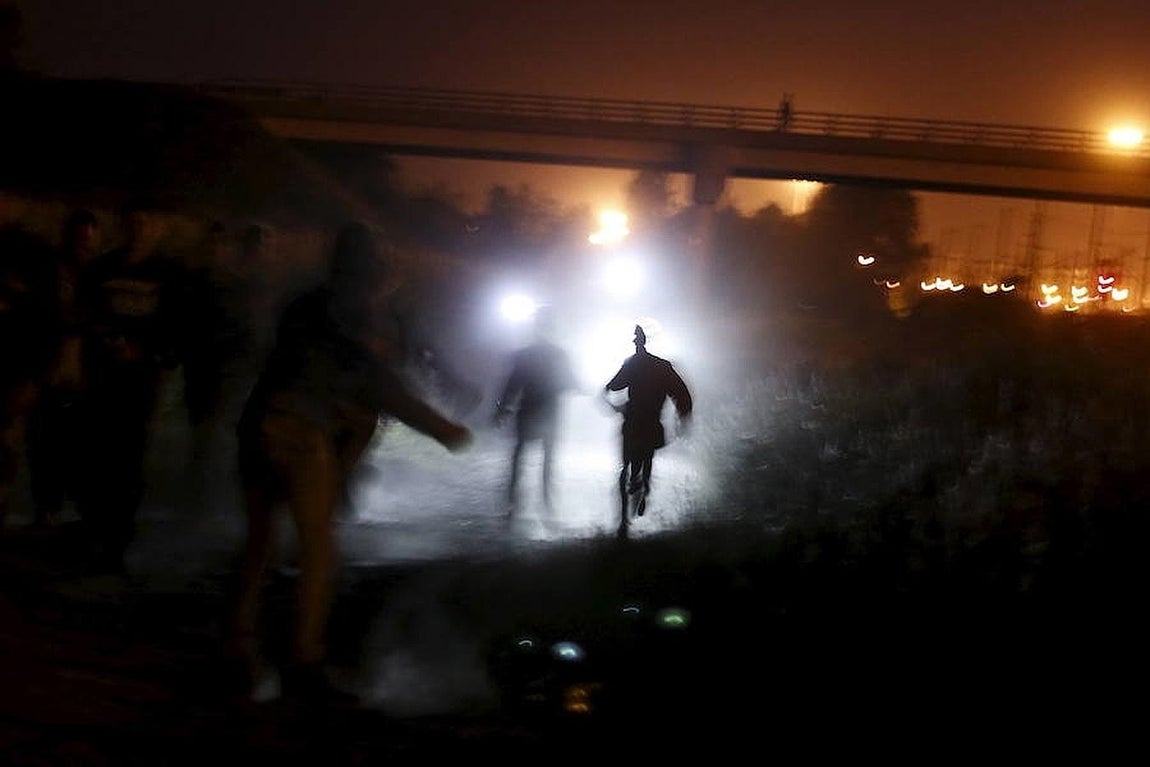 Varios migrantes son iluminados por antorchas de policía mientras corren para cruzar una valla durante un intento para acceder al túnel del Canal de Frethun, en Calais.. 
