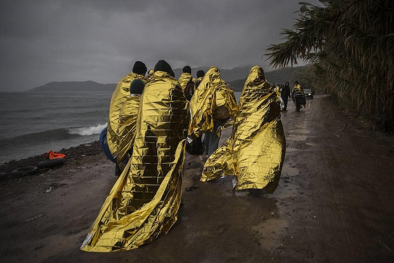 Un grupo de refugiados cubiertos con mantas térmicas abandona la playa de Skala Sikamineas a la que llegaron en patera, minutos antes, procedentes de las costas turcas