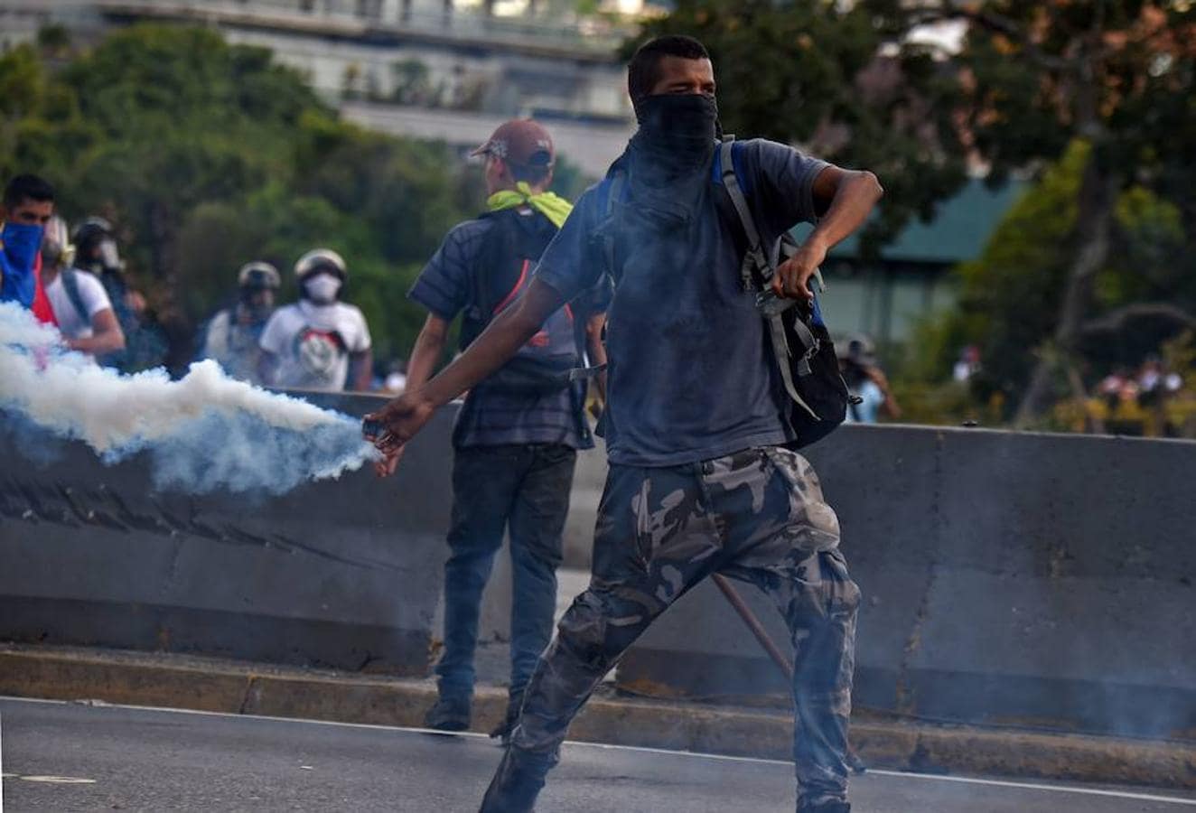 Un opositor lanza de nuevo una granada de gas lacrimógeno a la policía antidisturbios durante la marcha en Caraca