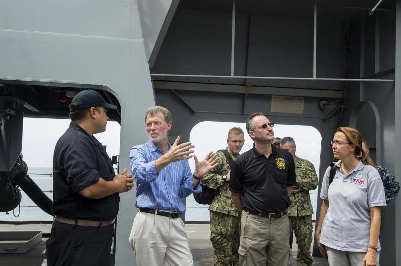Peter F. Mulrean (camisa azil), embajador estadounidense en Haití, recorre la nave del muelle de transporte anfibio USS Mesa Verde, destinado para distribuir suministros