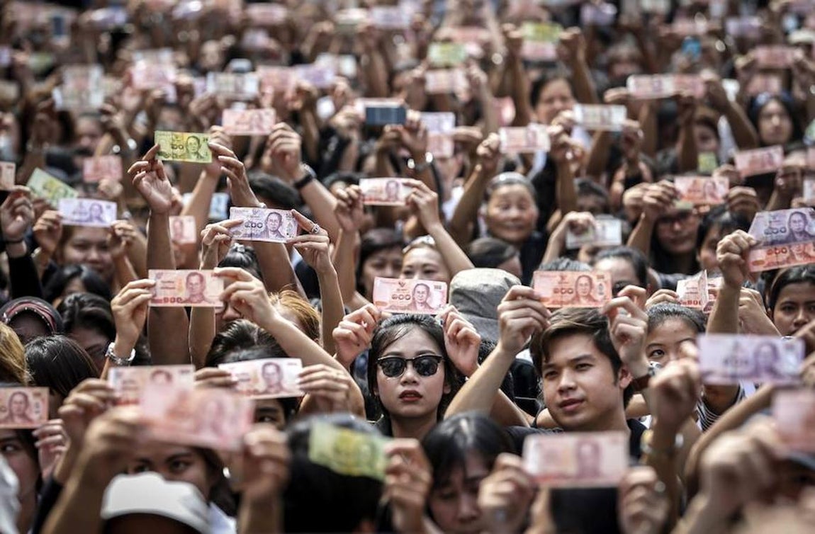 Tailandeses muestran billetes con la imagen del rey Bhumibol Adulyadej a la entrada del hospital Siriraj en Bangkok, donde el monarca falleció ayer a los 88 años de edad. Efe