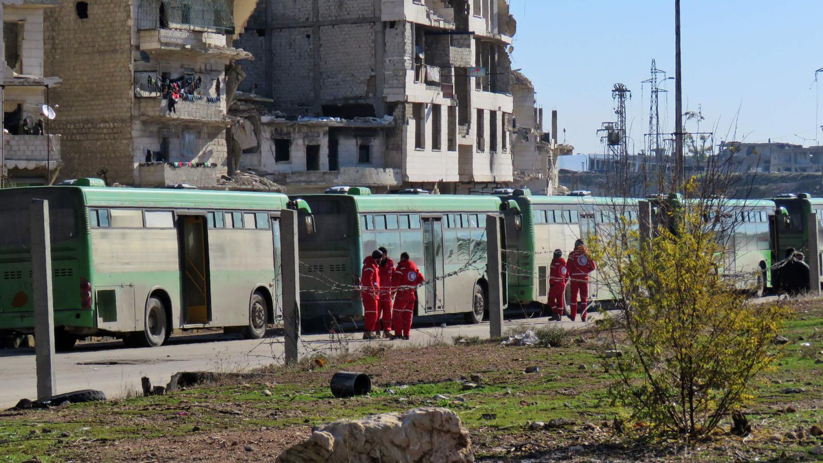 Un grupo de miembros de la Media Luna Roja espera junto a los autobuses preparados para evacuar a los rebeles sirios y sus familias de Alepo