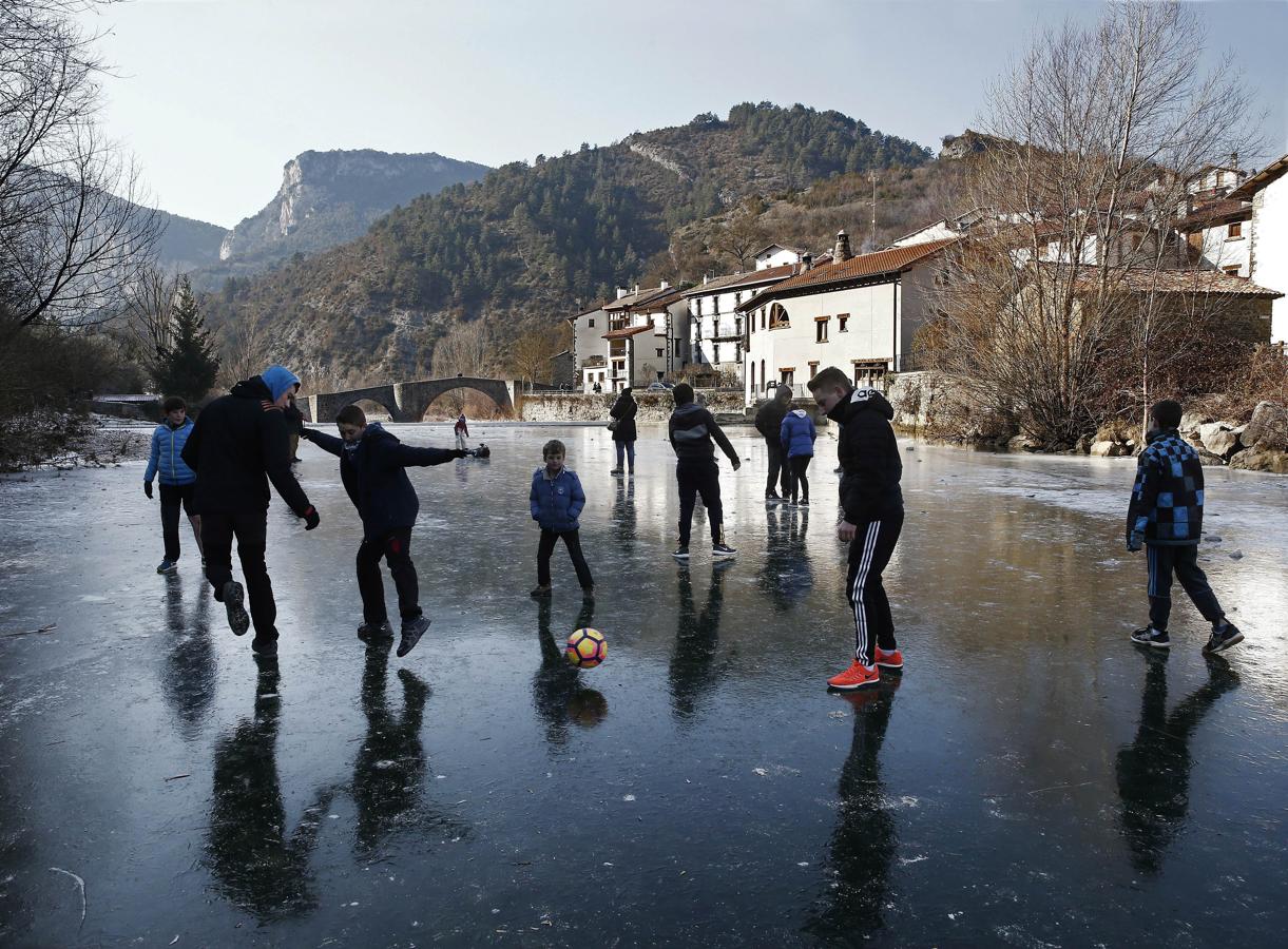 Un grupo de jóvenes juegan con un balón sobre la superficie helada del río Esca, en Burgui, Navarra, cuyo cauce amaneció con una capa de hielo de diez centímetros