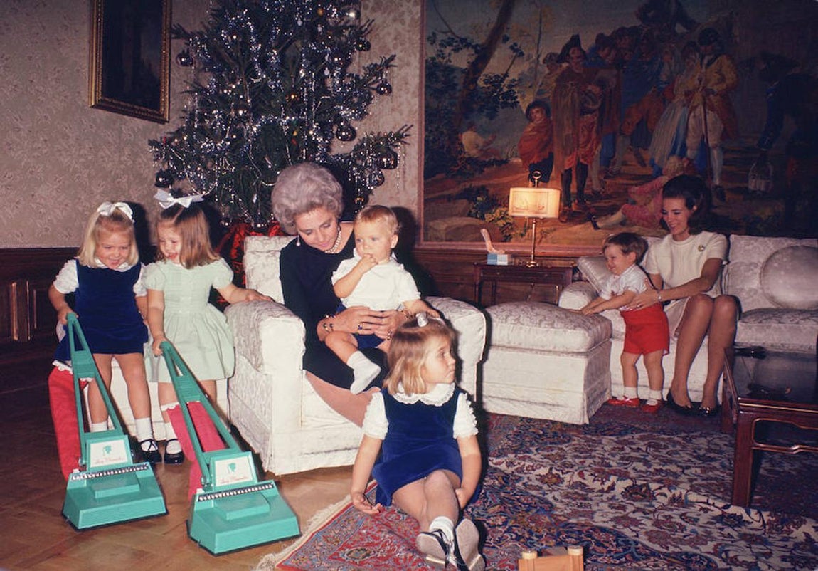 El Príncipe Felipe en brazos de la Reina Federica, con la Infanta Elena delante. La Infanta Cristina y su prima Alexia de Grecia juegan con unas aspiradoras de juguete. Al fondo, la Reina Ana María de Grecia con su hijo Pablo. 